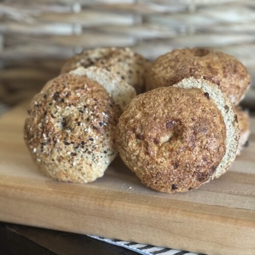 This image is of a wooden cutting board topped with cottage cheese bagels. There is a brown whicker basket in the background.