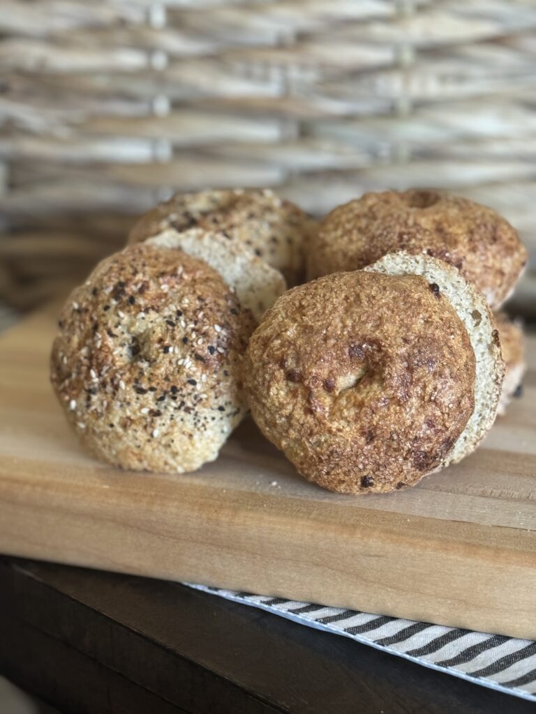 This is a picture of cottage cheese bagels on a wooden cutting board with a striped napkin underneath and a basket behind. 