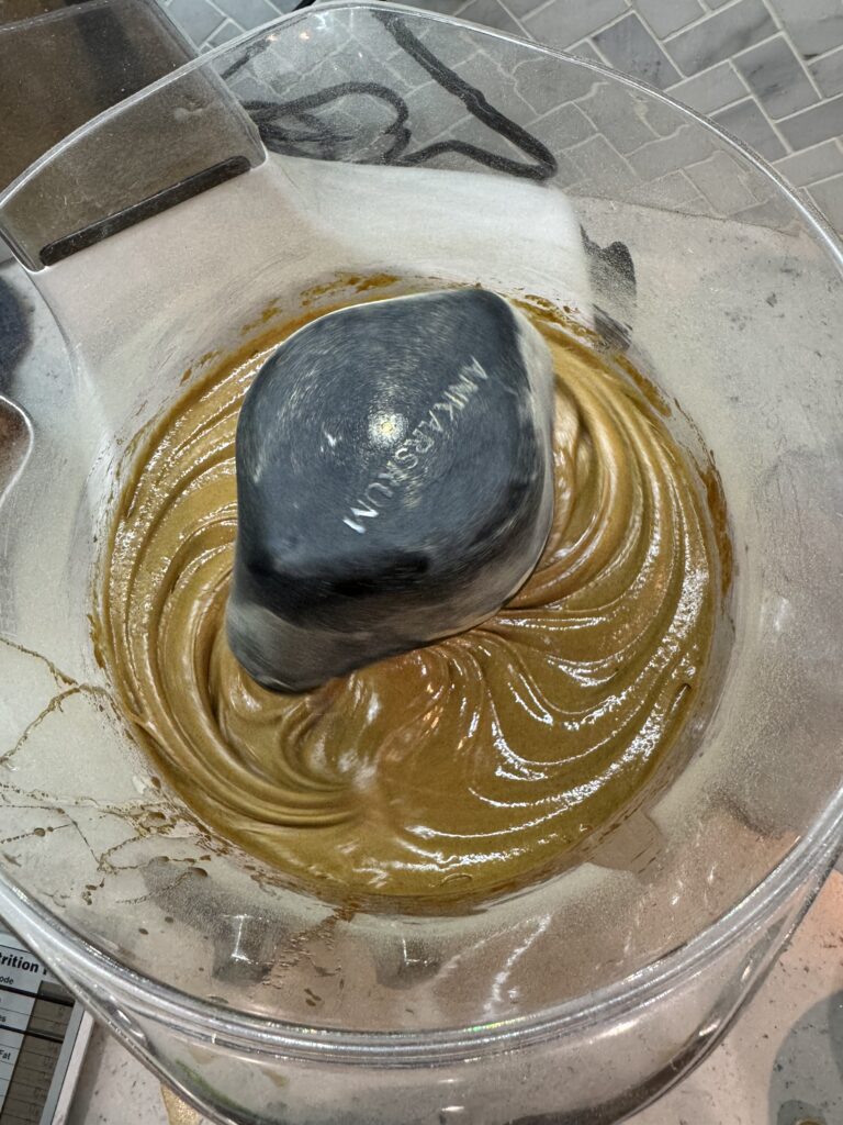 This image is of the inside of a clear plastic mixing bowl. There is a brown thick substance in the bottom. The top of the "Ankarsrum" brand label is visible on the top. This is the first step in making dark chocolate brownies.