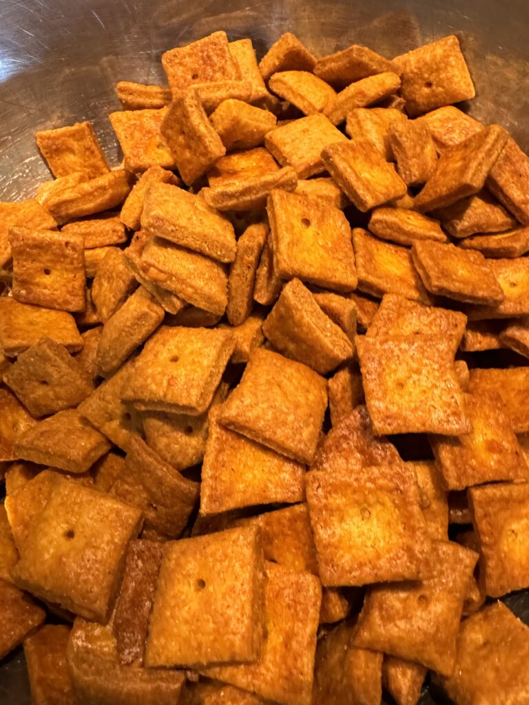 This image is a silver bowl full of baked cheese crackers made with fresh milled flour. They are light orange and darker orange around the edges.