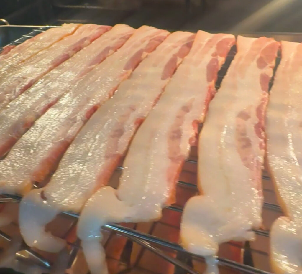 This image is of 10 slices of bacon draped over a wire rack going into a hot oven.