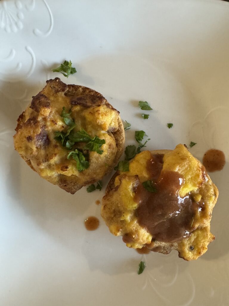 This image is of 2 english muffin breakfast sandwiches on a plate, one topped with salsa and the other topped with cilantro, chopped.