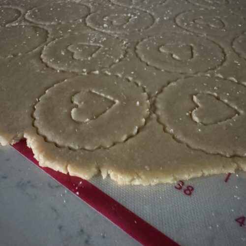 This image is of a silicone mat lined with red. It has cookie dough cut out with scalloped edges and a heart cut out.