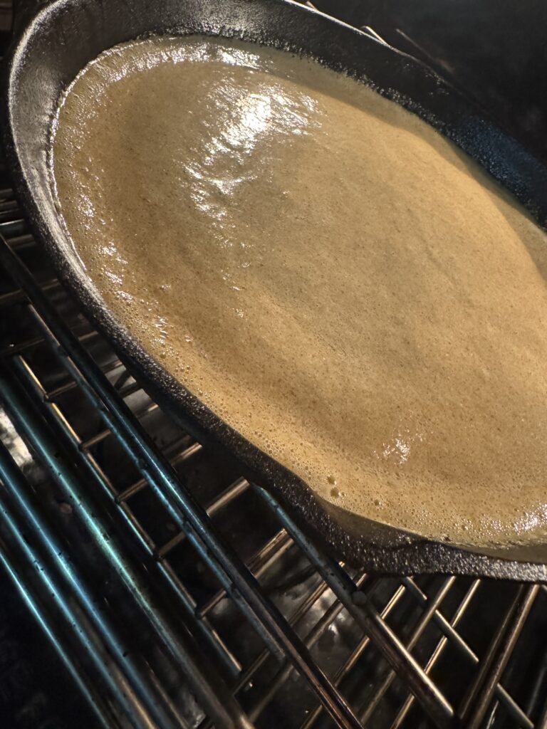 This image is of a cast iron skillet in an oven with cooking cornbread in it.