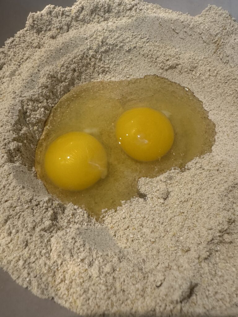 This image is of a white and yellow dry mixture in a bowl with 2 eggs in the center of the dry ingredients.