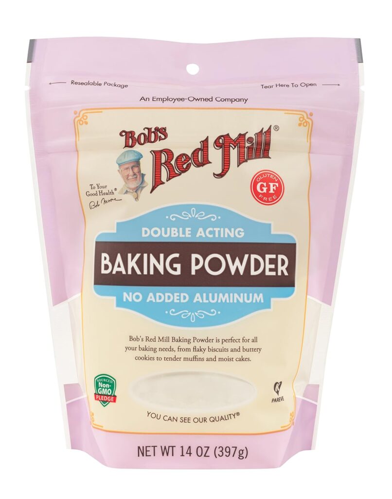 This image is of Bob's Red Mill Baking Powder. It is a pink bag, with wred writing, a blue section in the middle and a brown ribbon across the blue section stating the item is BAKING POWDER.