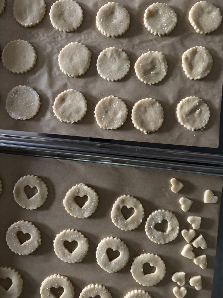 This image is of pans lined with tan parchment paper and topped with ivory round cookie dough circles with hearts cut out of the centers of some.