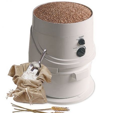 This image is of a white plastic grain mill filled with grains. There are black knobs on the front of the mill.