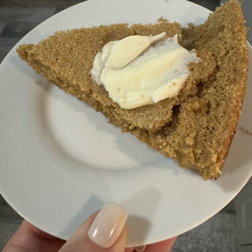 This image is of a white plate topped with cornbread. It is topped with butter.