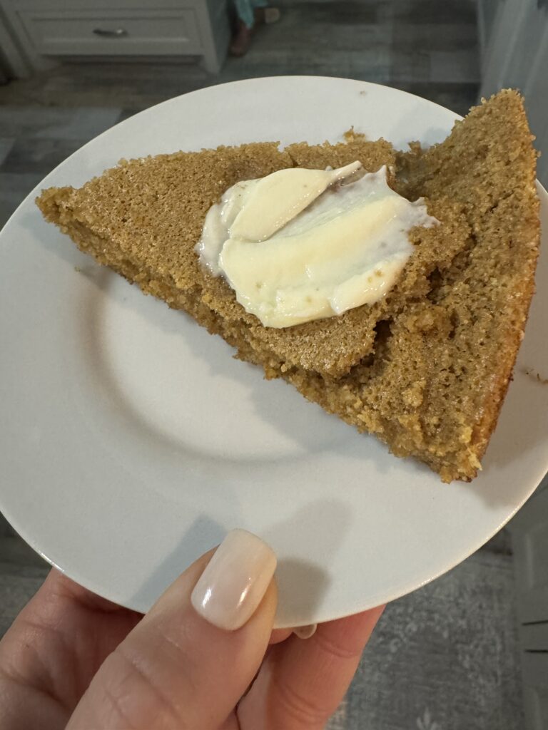 This image is of a white round plate and a slice of gluten free sorghum cornbread on top. it is topped with butter.