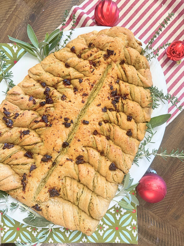 Christmas tree pesto bread on a platter surrounded by fresh herbs and christmas ornaments