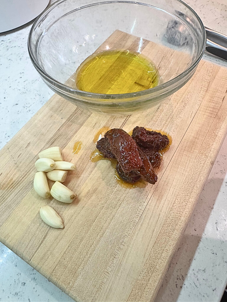 Toppings for christmas tree pesto bread on a wooden cutting board. Olive oil, sundried tomatoes and garlic cloves.