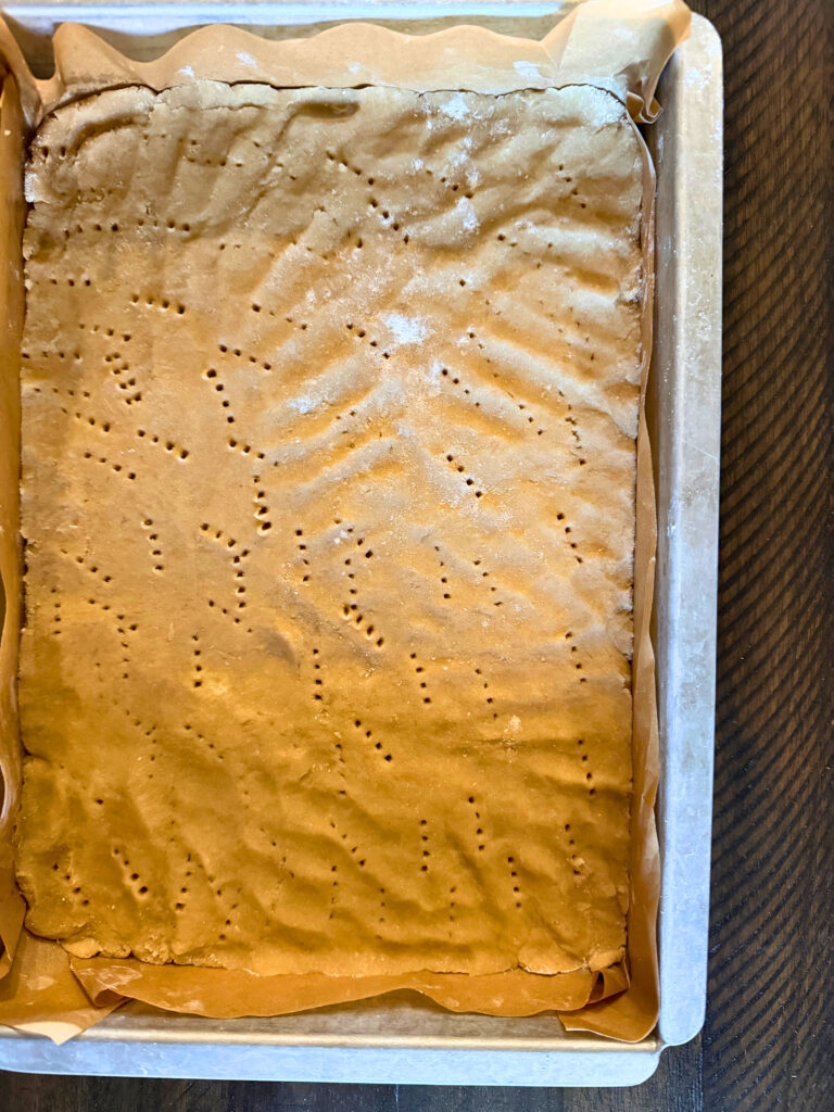 Lemon bar crust poked with a fork and in a rectangle metal pan